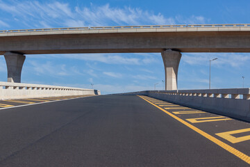 Naklejka premium Travel Route New Road Highway Exit Entry overpass lanes standing middle of empty ramp tarred asphalt road panoramic landscape with blue sky.