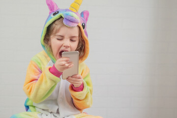 Little girl child in a unicorn costume holds a phone in his hand. Baby yawns