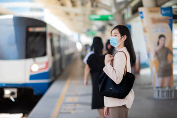 Asian woman wearing face mask, standing at gate station, waiting for metro or subway train