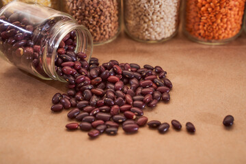 red bean beans crumbled from a glass jar on a brown background. Close up