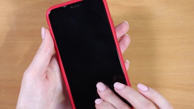Female hands hold a smartphone in a red case. Top view close up