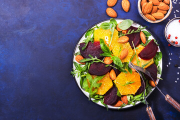 Fresh Beetroot Salad with Orange, arugula and almonds nut on blue background. Vegan healthy summer food. Flat lay. Copy space