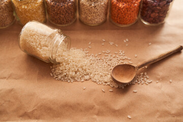 White rice is scattered on a brown background with a wooden spoon and against the other croup