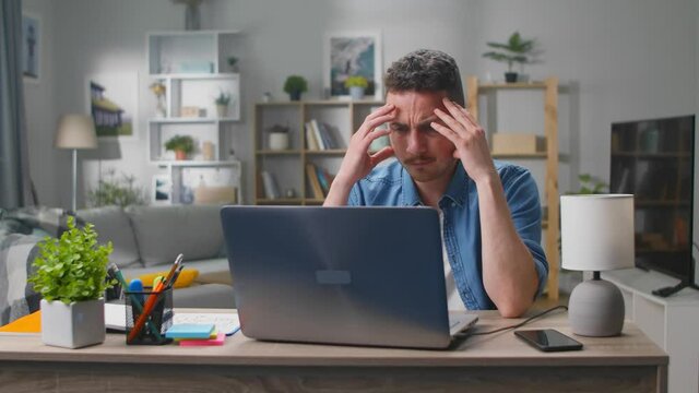 Confused young man thinks over a problem in the living room at the desk