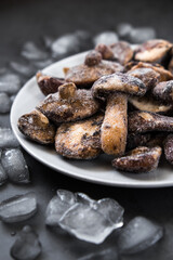 a white plate with frozen mushrooms covered with melting ice and hoarfrost. frozen green vegetables product. winter food preservation. cold from the freezer. dark vertical selective soft focus