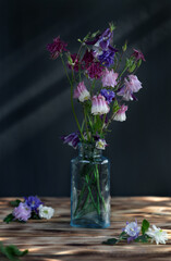 Multi-colored bouquet of flowers in a glass bottle on a wooden background