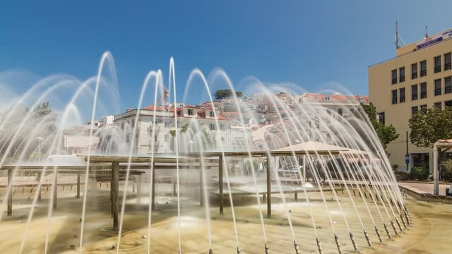 Fountain in Martim Moniz square timelapse hyperlapse in downtown Lisbon. Historic buildings on hills on a background with blue sky