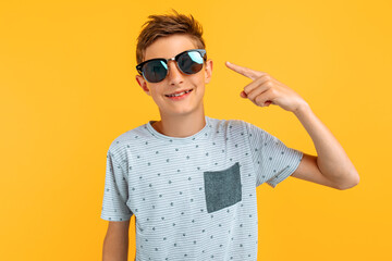 Beautiful stylish teen guy in sunglasses posing standing on an isolated yellow background