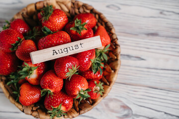 The inscription Augustus on the tree. Fresh juicy strawberries organic bio berries in a wicker basket on a rustic table.Eco, organic vegetarian summer diet food. Straw hat Sun glasses.