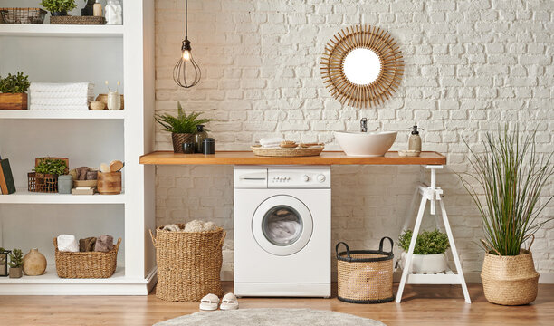 Washing machine in the laundry room, wooden table and shelf style, sink lamp mirror and wicker basket decor object.Laundry room interior style, washing machine wicker basket white bookshelf and sink.