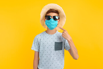 Fototapeta na wymiar teenager in a summer hat and sunglasses, with a protective medical mask on his face, on an yellow background
