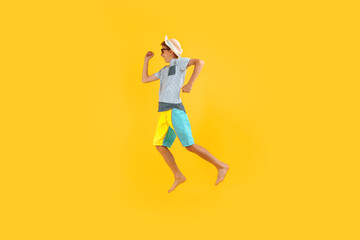 Fototapeta na wymiar happy excited teenager in sunglasses and a summer hat, having fun and jumping, on a yellow background