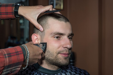 Fototapeta premium haircut of a young guy with a shield in a barbershop using a typewriter with a nozzle. Barbershop