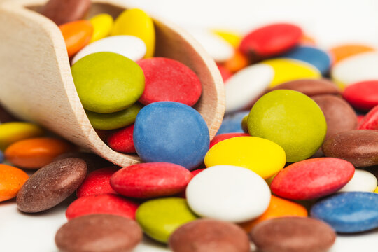Lentejas de chocolate de colores junto auna cuchara de madera sobre un fondo blanco. Vista de frente y de cerca. Macro