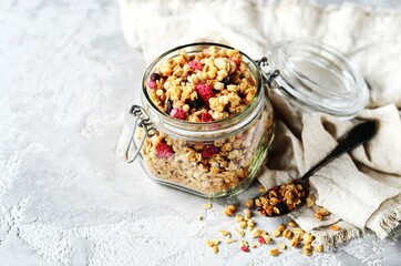 Homemade granola with berries and nuts in a glass jar on a gray background
