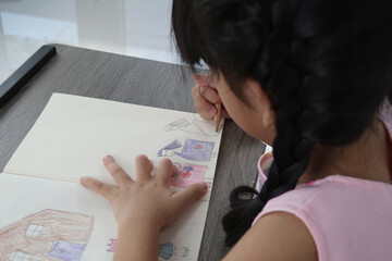 Young girl is drawing people and coloring on her note book  on the table .