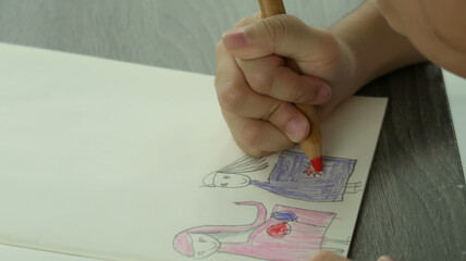 a girl right hand is coloring on her drawing picture with orange pencil. 
