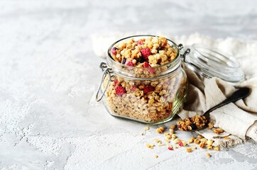 Homemade granola with berries and nuts in a glass jar on a gray background