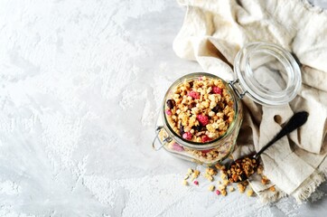 Homemade granola with berries and nuts in a glass jar on a gray background