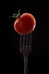 Tomato on a fork with drops and splashes of water.