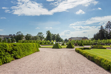 Uppsala, Sweden - 16 June 2019: Beautiful green park with green pyramids of trees and a fountain, in front of the building Linneanum orangery. One of the oldest botanical gardens in the world.