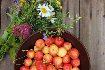 Yellow and pink cherries in a bowl, and midsummer wild flowers on a vintage wooden board background. Summer composition

