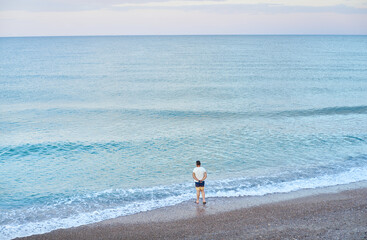 Person thinking on the shore of the beach in the Mediterranean sea without waves at sunset with blue, pink and mauve colors