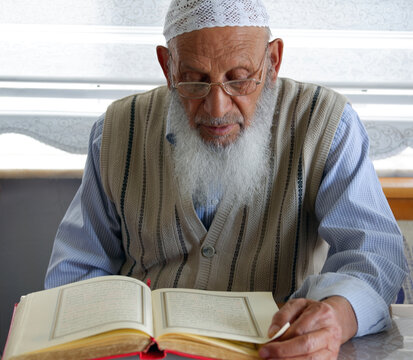 Close-up of an Elderly Muslim Turkish Man's face who is reading Holy Quran during Ramadan. Grandfather with glasses and white beard reading holy book. Selective Focus.