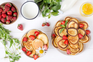 Trendy home breakfast with mini pancakes and strawberry on white table. View from above.