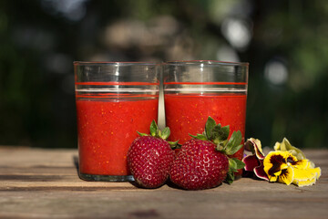 Strawberry juice with glass glasses on a wooden table and on the background of a green garden, on the table are ripe strawberries. Useful food, background