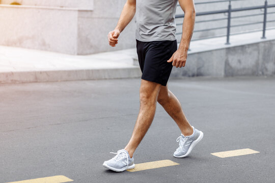 Fitness man athlete runner walking on the road. Person running working out living an active lifestyle training cardio in summer in sportswear and shoes. Lower body banner crop. Close up.