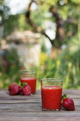 Strawberry juice with glass glasses on a wooden table and on the background of a green garden, on the table are ripe strawberries. Useful food, background, place for text.
