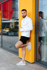 Sports. Portrait of strong healthy handsome Athletic Man Fitness Model posing near yellow wall. Attractive athlete resting after workout outdoors, fitness and healthy lifestyle concept.City background