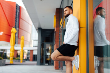 Fototapeta na wymiar Sports. Portrait of strong healthy handsome Athletic Man Fitness Model posing near yellow wall. Attractive athlete resting after workout outdoors, fitness and healthy lifestyle concept.City background