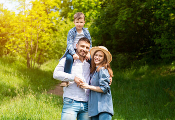 Portrait of loving parents with their little son standing together in forest on sunny day