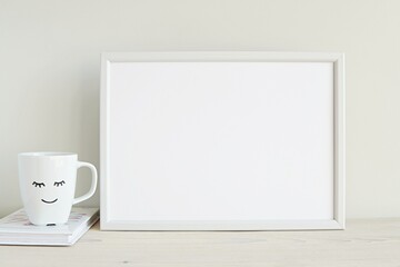 Fototapeta na wymiar Blank white frame mockup for artwork display, cup with smile, white interior.