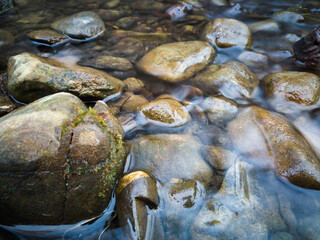 Stones protrude from the water in a small hilly stream.
