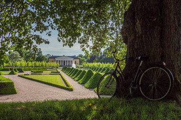 Uppsala, Sweden - 16 June 2019: Beautiful green park with green pyramids of trees and a fountain, in front of the building Linneanum orangery. One of the oldest botanical gardens in the world.