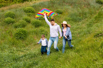 Fun family pastimes. Young parents with their kid flying kite together on green meadow