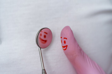 Finger in pink gloves with red smile on it. Looking to the dentist`s mirror.