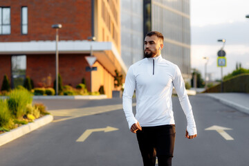 Fototapeta premium Young Athletic man walking on the street against the background of modern buildings in the city. After workout sesion. After running. Healthy, lifestyle concept.