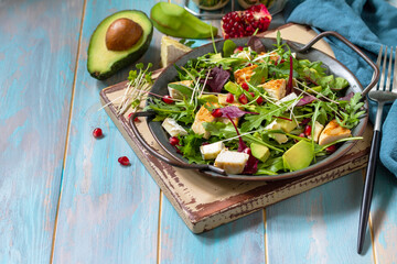 Arugula salad with chicken, avocado, pomegranate and cheese on wooden table. Copy space.