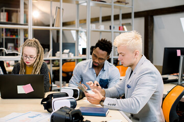 Handsome concentrated man, business worker, sitting in office room during meeting and using ipad tablet. Handsome African man and blond Caucasian girl with dreadlocks working on the background