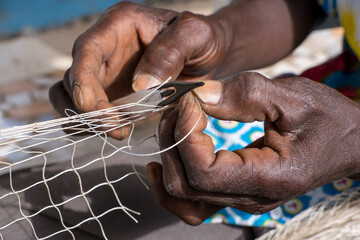 Imagen con unas manos reparando una red de pesca en el pueblo de Joal Fadiouth en la costa de...