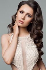 Portrait of beautiful brunette wearing in shine dress with long hair, perfect skin after beauty salon. Woman with professionally haircut, long eyelashes and evening make up seductive posing at camera.