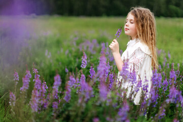 A little girl in a white dress with beautiful flowers in the field in summer. Concept of happy childhood. Copy space for text