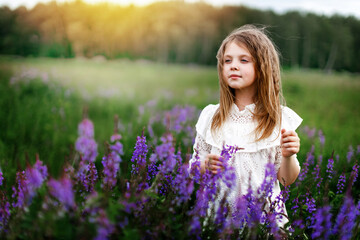 A little girl in a white dress with beautiful flowers in the field in summer. Concept of happy childhood. Copy space for text