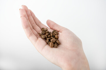 Woman's hand holding medium roasted coffee beans on isolated white background