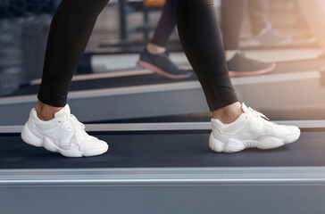 Unrecognizable woman in sports shoes walking on treadmill at gym, closeup of legs