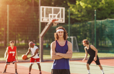 Portrait of positive basketball player and his team playing ball at outdoor court
